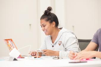 Student wearing Texas Longhorns hoodie smiling as she works on a project in a studio design course with IBM