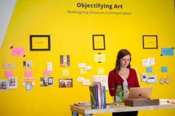 MFA candidate stands in front of her MFA exhibition, Objectifying Art
