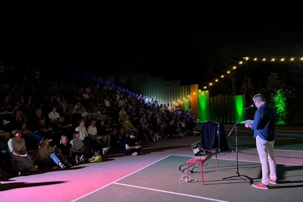 Audience seated in a darkened auditorium watching a PechaKucha presentation projected on screen, with speakers silhouetted against the stage lighting.