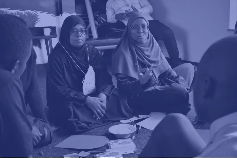 Coast Region Director of the Madrasa Early Childhood Programme Masad Omar (left) and Halima Shaaban, the Schools2030 National Coordinator for Kenya (right), engaging with students at the Train the Trainer in Design Thinking working held in Nairobi, Kenya, February 2020. two teachers wearing hijabs sit on the ground during a workshop with Katie Krummeck and Gray Garmon