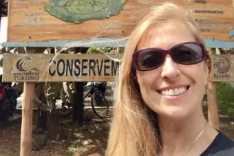 Natacha Poggio smiles in front of a sign that reads "Welcome to San Cristobal"