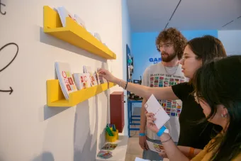 Three Becauseisms attendees taking program guides from a shelf on the wall