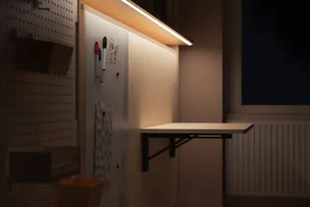 A folding desk unit with shelves and a white board, with a dim light illuminating the workspace. 