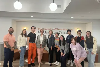 A group photo of UT Austin students posing with Patti DeNucci in front of the Kendra Scott Center sign