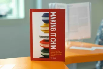 Close-up of the book “Making It Chin: Sustaining Chin Identity in the USA Through Everyday Designs” by Van Thang, displayed upright on an orange table at a design exhibition.