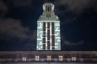 The UT Austin Tower at night lit with a projection mapping display of a retro-style video game, featuring blocks, ladders, and characters.