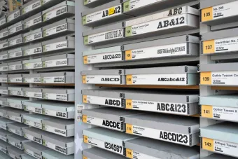 Rows of flat storage drawers are meticulously labeled with wood typeface names, point sizes, and examples of printed characters. The drawers—stacked floor to ceiling—form a dense, typographic archive that reflects the scope of the Rob Roy Kelly American Wood Type Collection.