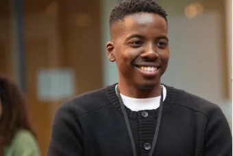 A smiling person with arms crossed at a professional event or workshop.