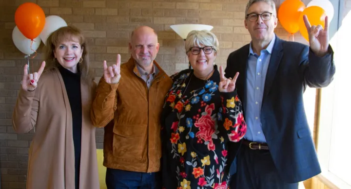 Karl and Nelda Buckman smile and throw up "hook 'em horns" hand signs alongside members of the College of Fine Arts development team at UT Austin
