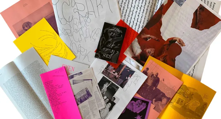 An assortment of zines and printed materials spread out in an overlapping arrangement. The collection includes various colors such as bright pink, yellow, orange, and red, along with black-and-white pages. Some zines feature handwritten elements, abstract illustrations, and photographs, including an image of a person wearing red and another of a group of people. The text on the covers and pages suggests themes of queer archival work and artistic expression.