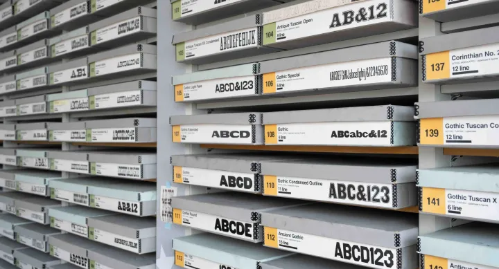Rows of flat storage drawers are meticulously labeled with wood typeface names, point sizes, and examples of printed characters. The drawers—stacked floor to ceiling—form a dense, typographic archive that reflects the scope of the Rob Roy Kelly American Wood Type Collection.