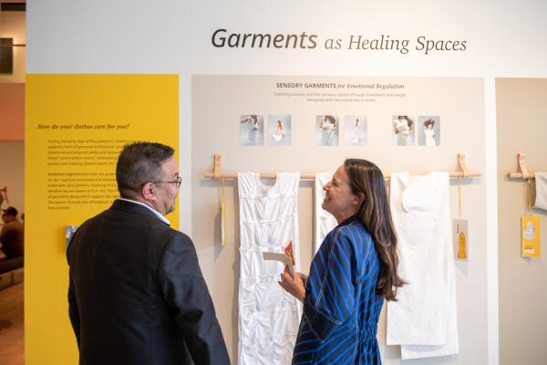 Two people laughing as they observe MFA design 2023 exhibit Garments as Healing Spaces at The University of Texas at Austin
