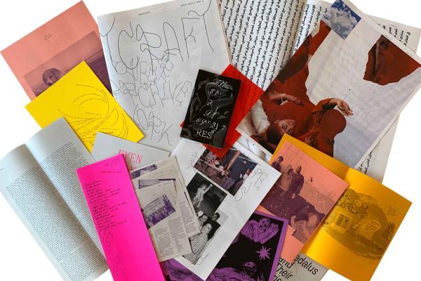 An assortment of zines and printed materials spread out in an overlapping arrangement. The collection includes various colors such as bright pink, yellow, orange, and red, along with black-and-white pages. Some zines feature handwritten elements, abstract illustrations, and photographs, including an image of a person wearing red and another of a group of people. The text on the covers and pages suggests themes of queer archival work and artistic expression.