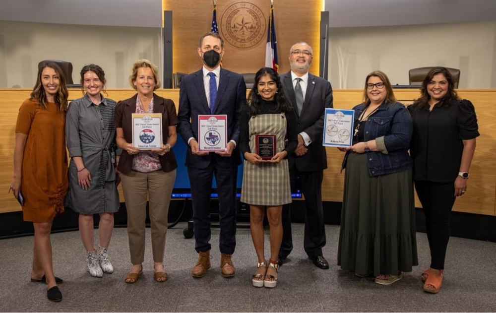 Ashwara Pillai, first place winner of the first Travis County "I Voted" sticker design contest, standing next to members of the Travis County Clerk Elections Division 