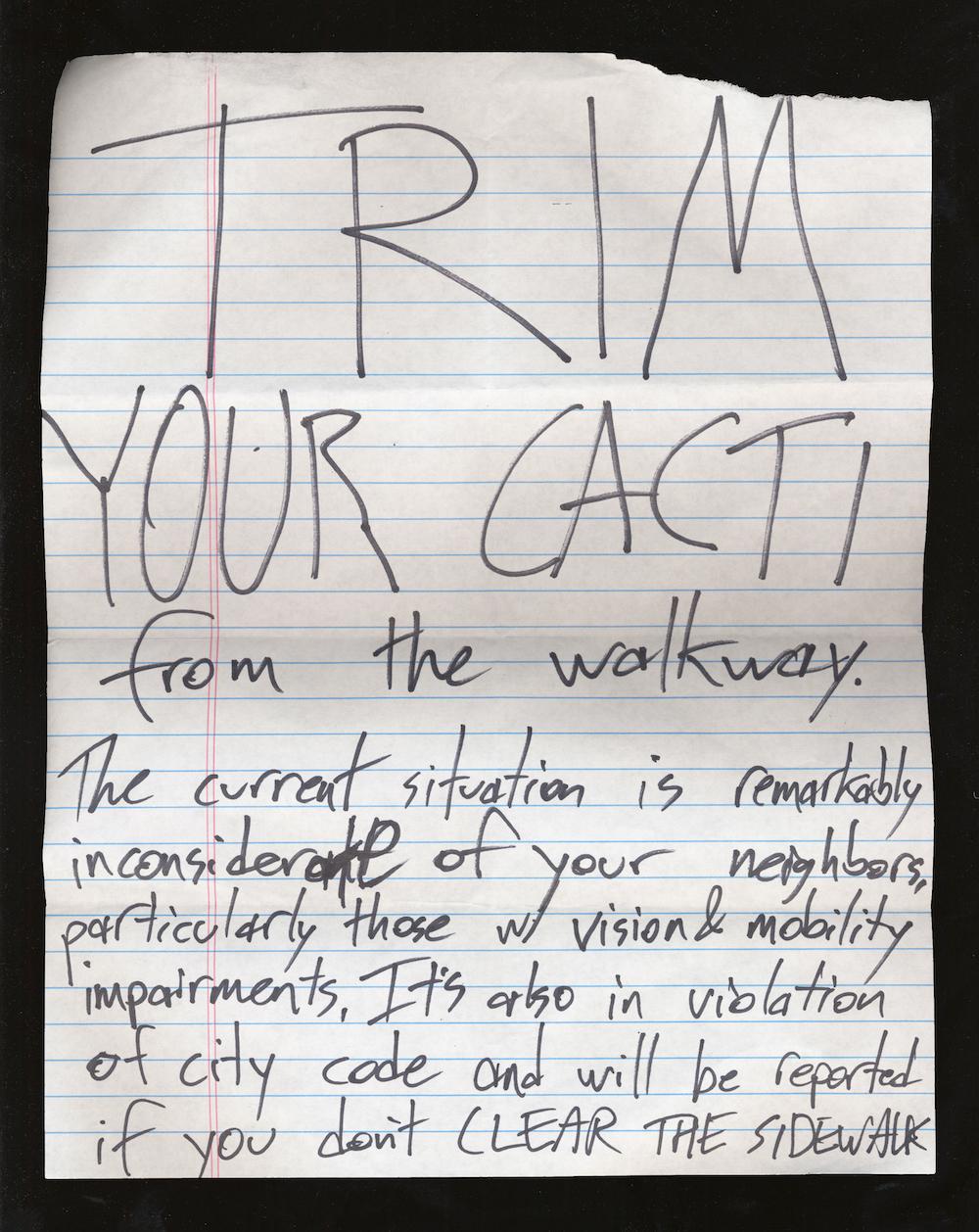 A note that reads TRIM YOUR CACTI from the walkway. The current situation is remarkably inconsiderate of your neighbors, particularly those with vision & mobility impairments. It’s also in violation of city code and will be reported."