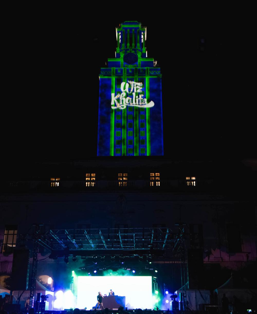 Image of UT Tower at night with Wiz Kalifa projection on it while the artist performs in front of the Main Building