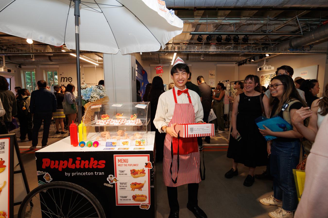 Student standing with their final project - a creative hotdog stand
