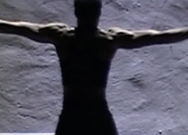 African American man with arms outstretched facing a rock wall with back to camera