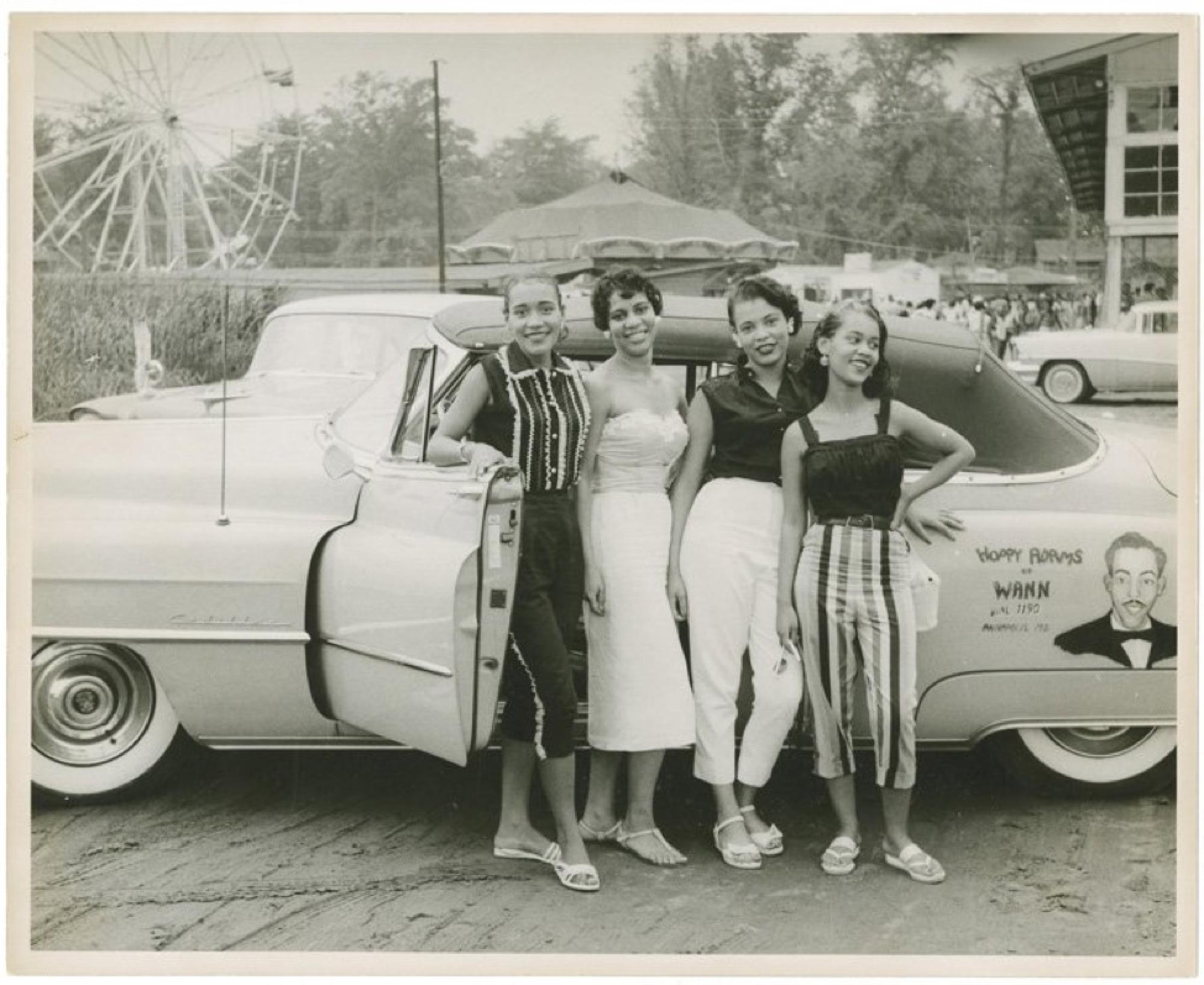 Source: https://americanhistory.si.edu/blog/negro-motorists-green-book 1960s Black and white photo of four Black women standing outside of a classic car at a carnival