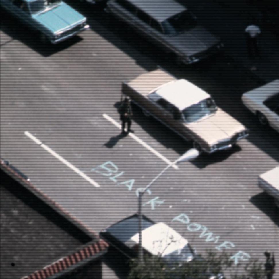 1967 color photo of cars on a highway. a man stands in the middle of the street next to the words Black Power written in chalk
