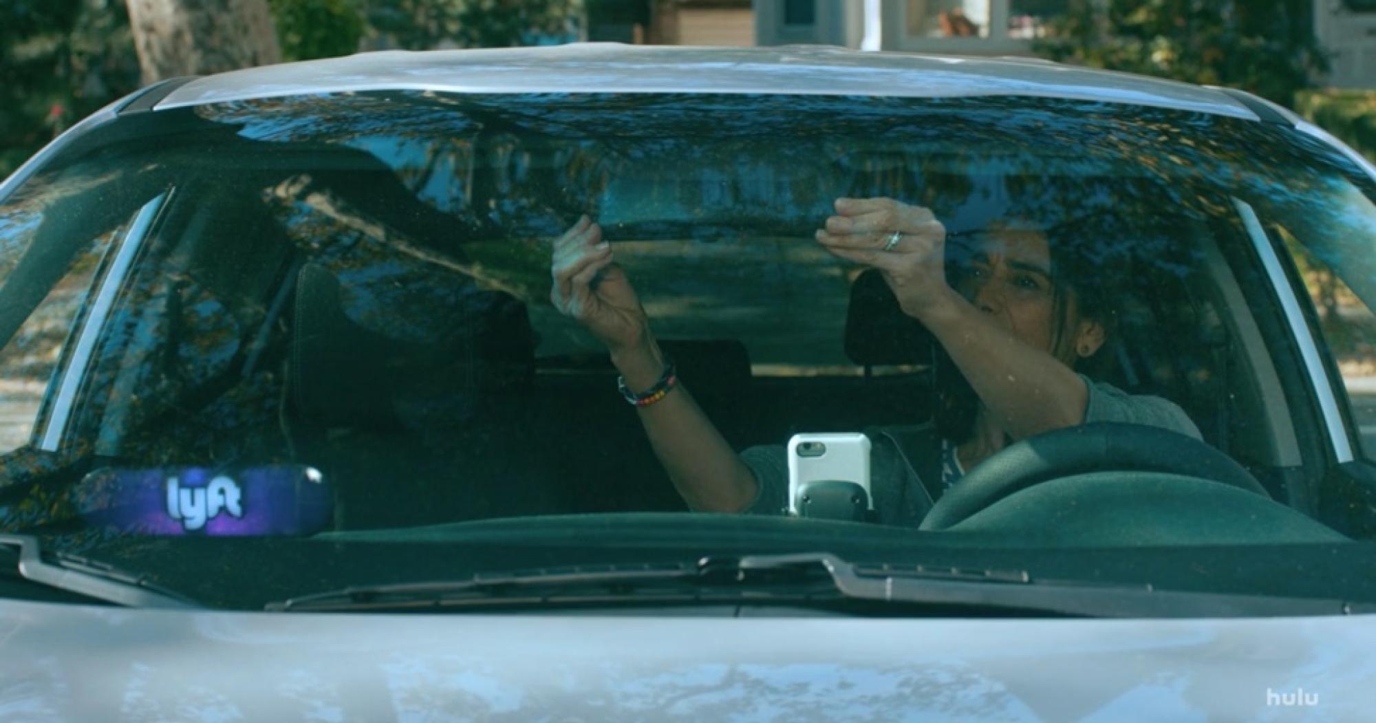 still image from TV series Ramy. a woman adjusts the rear-view mirror in her car. a Lyft logo is visible in the lower left corner of the windshield