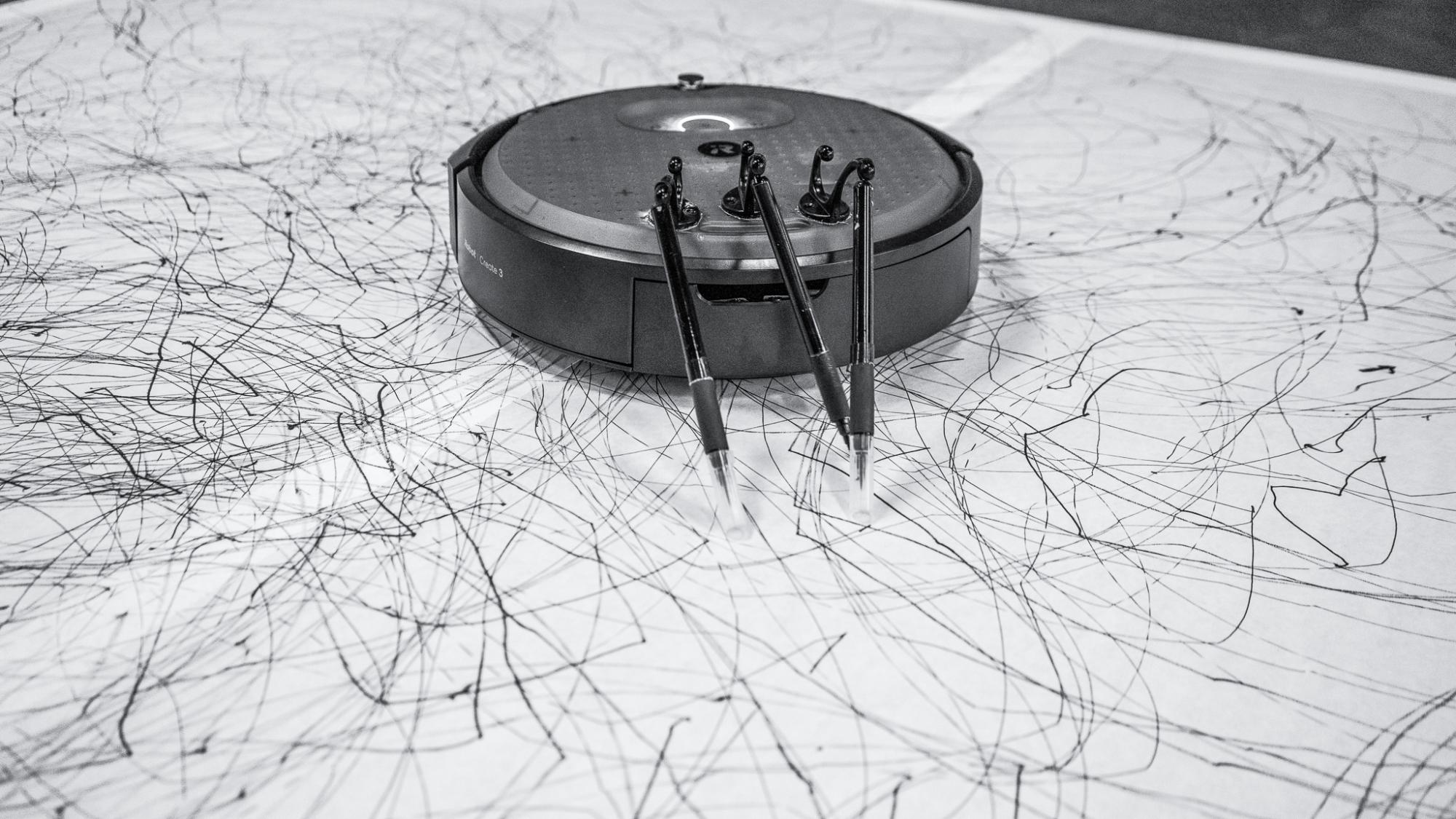 Roomba vacuum with pens drawing on large sheet of paper on the floor