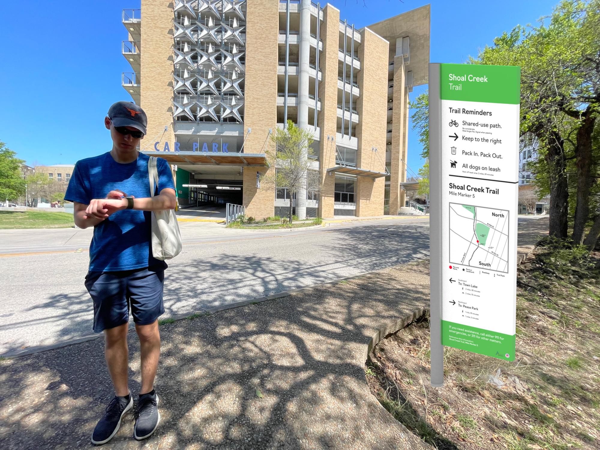 Student standing at the start of a trail path next to a mockup of a trail map
