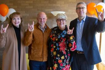 Karl and Nelda Buckman smile and throw up "hook 'em horns" hand signs alongside members of the College of Fine Arts development team at UT Austin