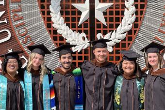 Six SDCT Design Graduates in cap and gown standing in front of UT Seal