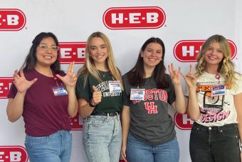 M.F.A. in Design alumna Chloe Gillmar wearing her Texas Design shirt and throwing up a "hook 'em" with her fellow H-E-B Digital interns from other Texas universities