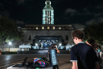 Photo of student playing "Tower Tumble," an original video game designed by AET students and faculty, on the UT Austin Tower through projection mapping