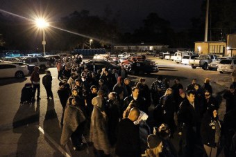 A crowd of people waiting in line to get into a pop-up clinic. It is dark outside, and most of them are wearing hoodies or blankets to keep warm. 