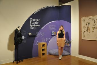 2022 MFA Design graduate Chloe Gillmar posing next to her exhibition Trauma Bonds