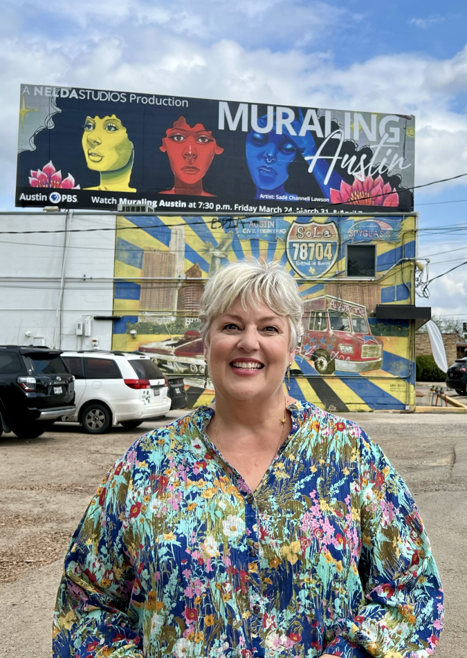 Nelda Studios founder Nelda Buckman smiling in front of a billboard advertising Muraling Austin