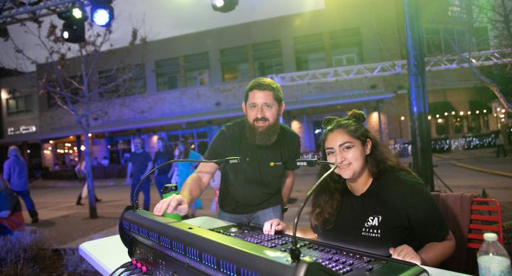 Arts and Entertainment Technologies professor Matt Smith and student Jayden Chavez smile at the camera while programming lighting at the 2022 Bee Cave BuzzFest