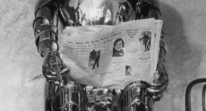 black and white photo of tin man sculpture reading a newspaper